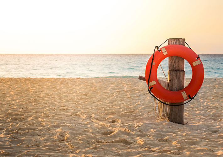Hilfe bei Schlaganfall Bild am Strand mit Rettungsring am Pfeiler im Sand steckend hängend